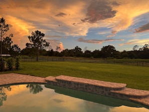 A swimming pool with a stone border, surrounded by a grassy area and a fence. - Waterski & More - Southwest facing pool (Clermont)