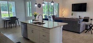 A modern kitchen with a central island, a dining area with a table and chairs, a gray sofa, and a flat-screen TV mounted on the wall. - Waterski & More - Southwest facing pool (Clermont)