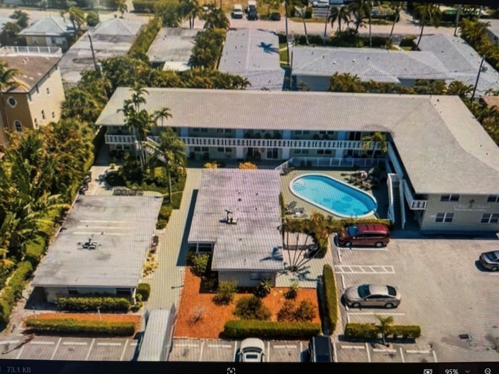 Vue aérienne d’un hôtel avec une piscine, un parking et des espaces verts environnants.