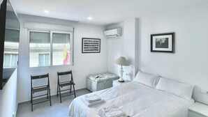 Un dormitorio con una cama grande, una silla, una mesita y una ventana con persianas.