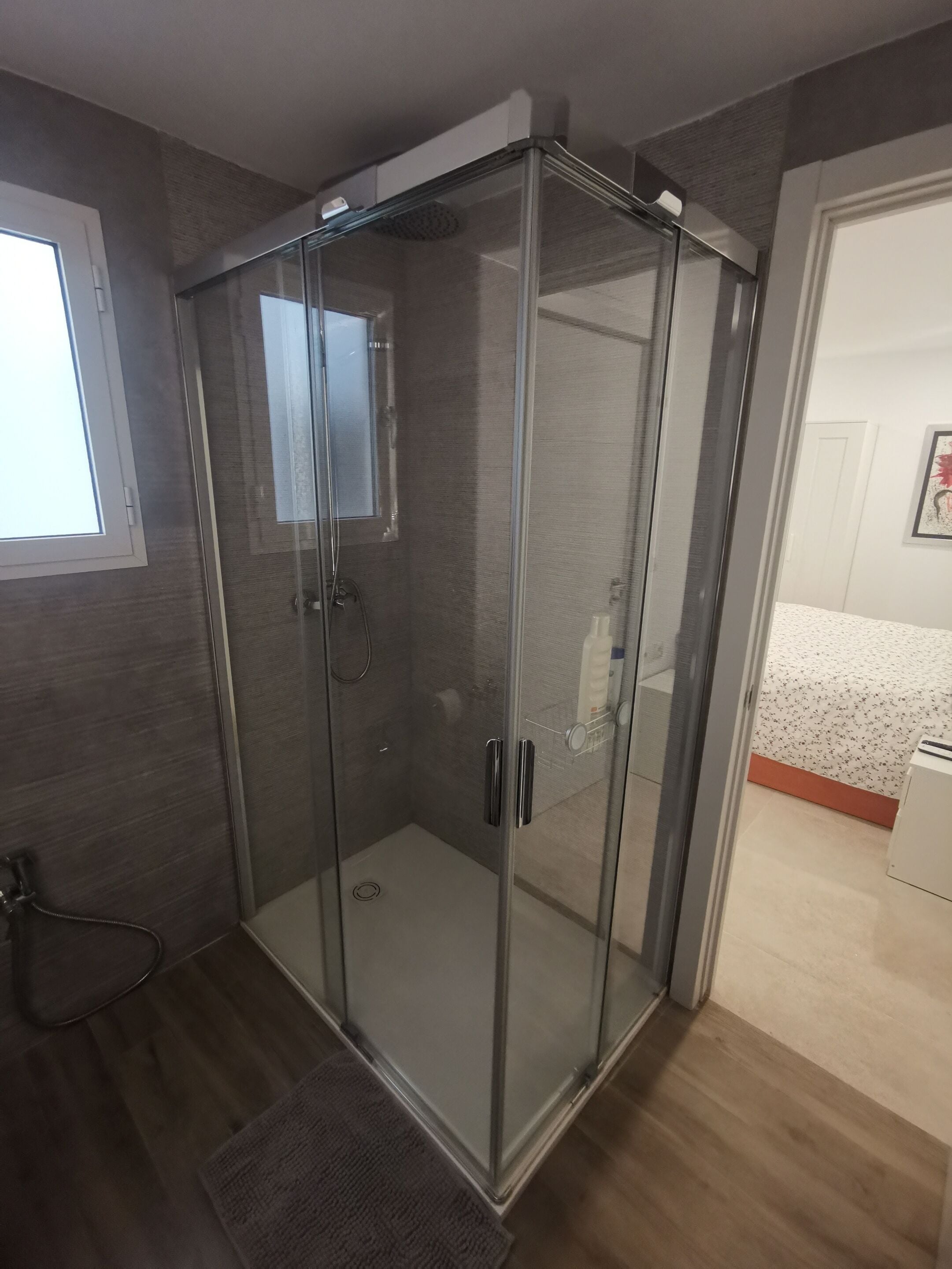 A glass-enclosed shower room with a door, a window, and a towel rack.