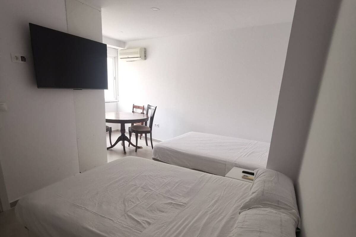 A hotel room with two beds, a TV mounted on the wall, and a small table with chairs.