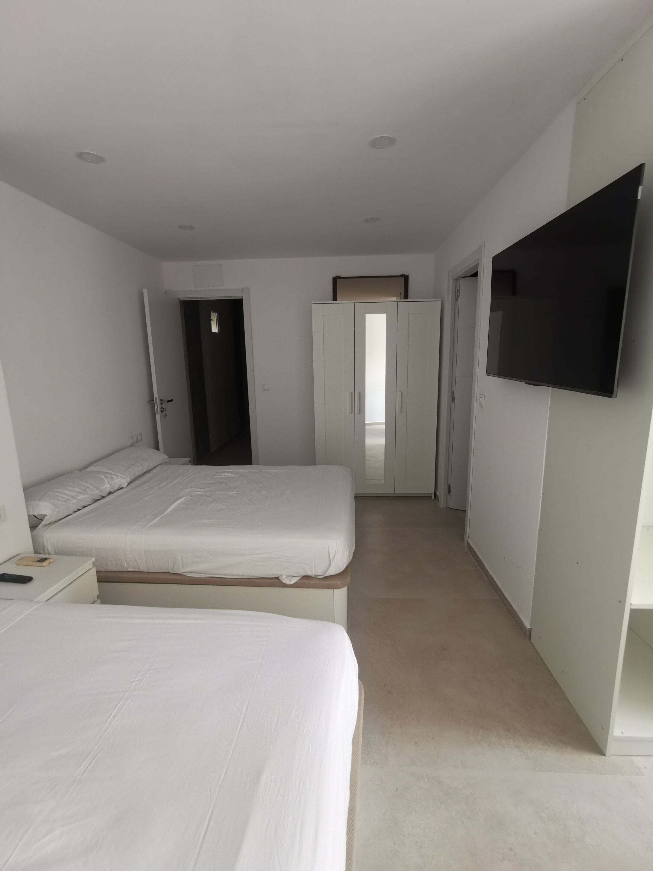 A room with two beds, a wardrobe, a television, and a door leading to another room.