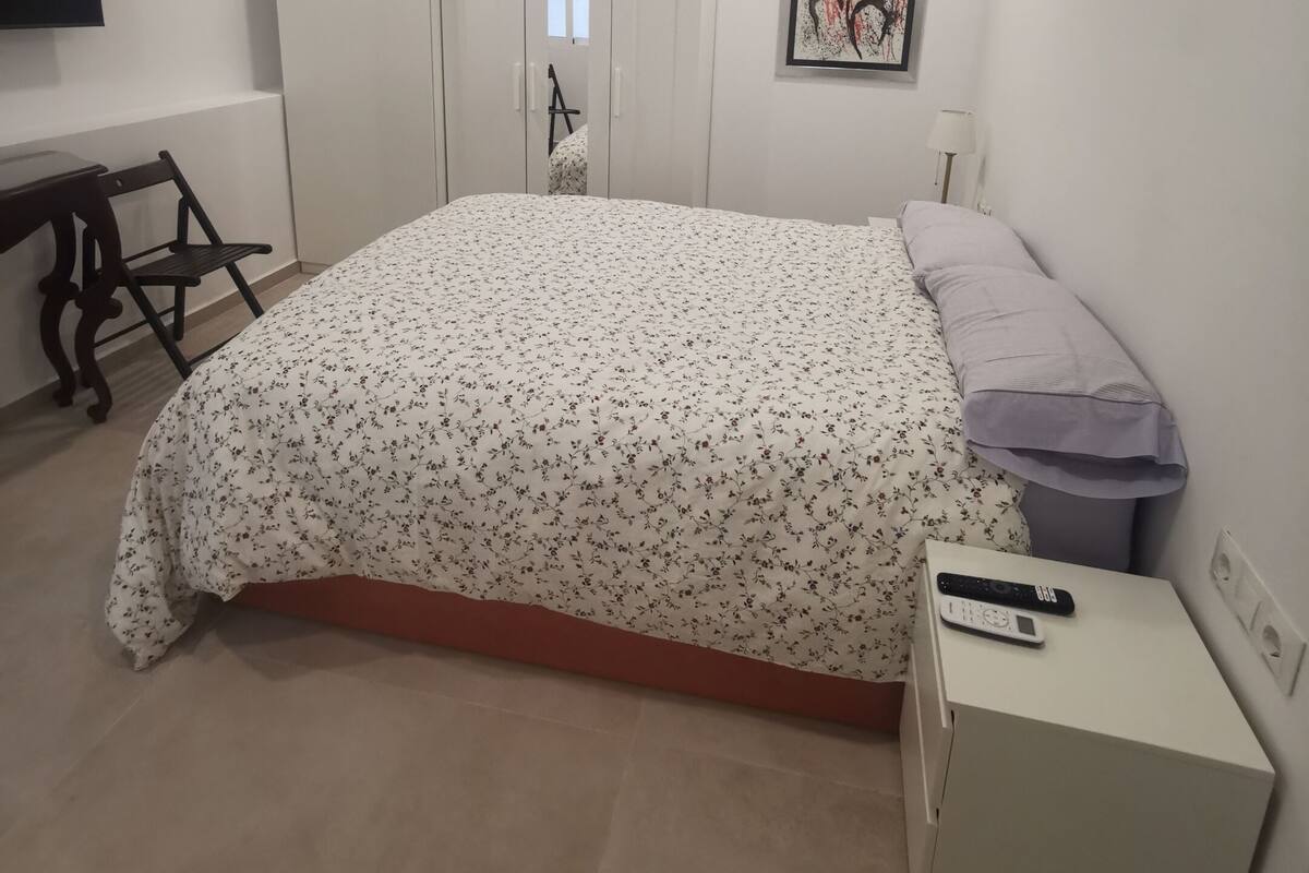 A bedroom with a bed, a nightstand, a TV, a wardrobe, and a door leading to another room.