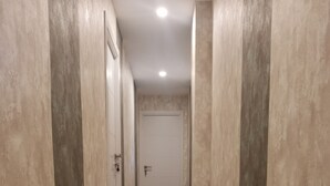 Un pasillo con paredes color beige y piso de tonos claros, que conduce a una puerta cerrada al final.