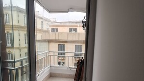 Un balcón con vistas a edificios vecinos, una lámpara colgante y una mesa con mantel de encaje.