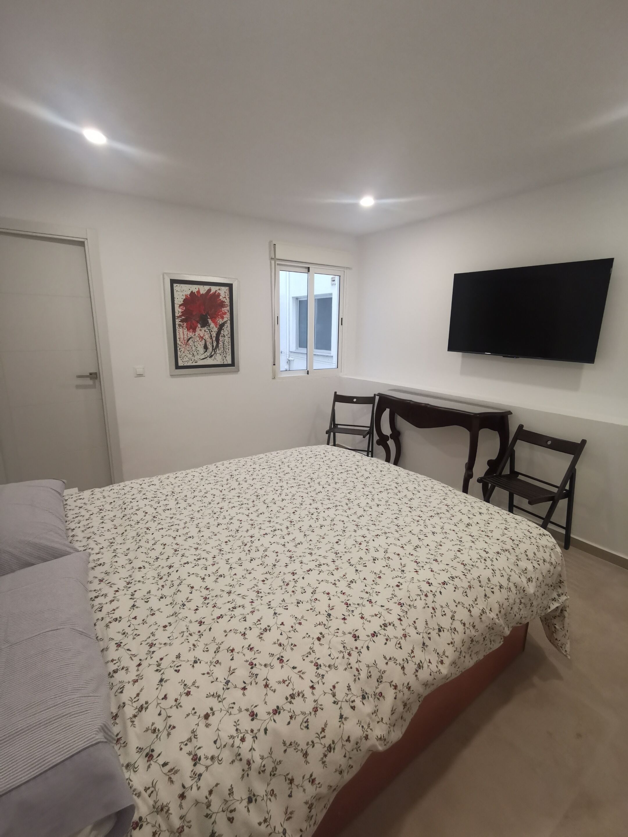 A bedroom with a bed, a desk, a chair, a TV, and a window.