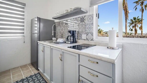 A compact kitchen with a refrigerator, a coffee maker, and a window with a view of palm trees. - Cozy 2-bedroom apartment with AC, WiFi in charming Cabo San Lucas (Cabo San Lucas)