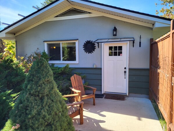 A house with a white door, a window, and a small porch area with a wooden chair. - Backyard Guesthouse near Nelson w/ Hot Tub (Nelson)