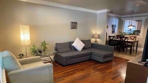 A living room with a grey sectional sofa, a white armchair, and a glass coffee table. There is a dining area with a wooden table and chairs. - Clean, quiet, centrally located home (Salt Lake City)