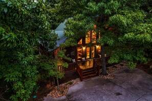 A wooden cabin with a porch, surrounded by dense foliage. - Peaceful private, King Bed, hot tub, arcade, minutes to attractions and parkway (Sevierville)