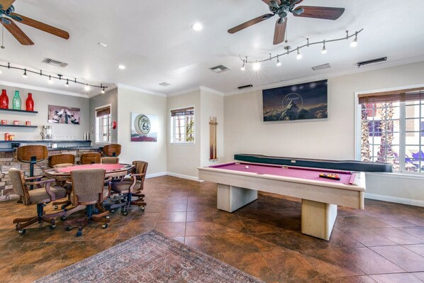 A spacious room with a pool table, a dining area with chairs, a ceiling fan, and a large window with blinds. - Havasu Mulberry - 5Min Walk To Beach, Pool, Spa, Game Room, FirePit (Lake Havasu City)