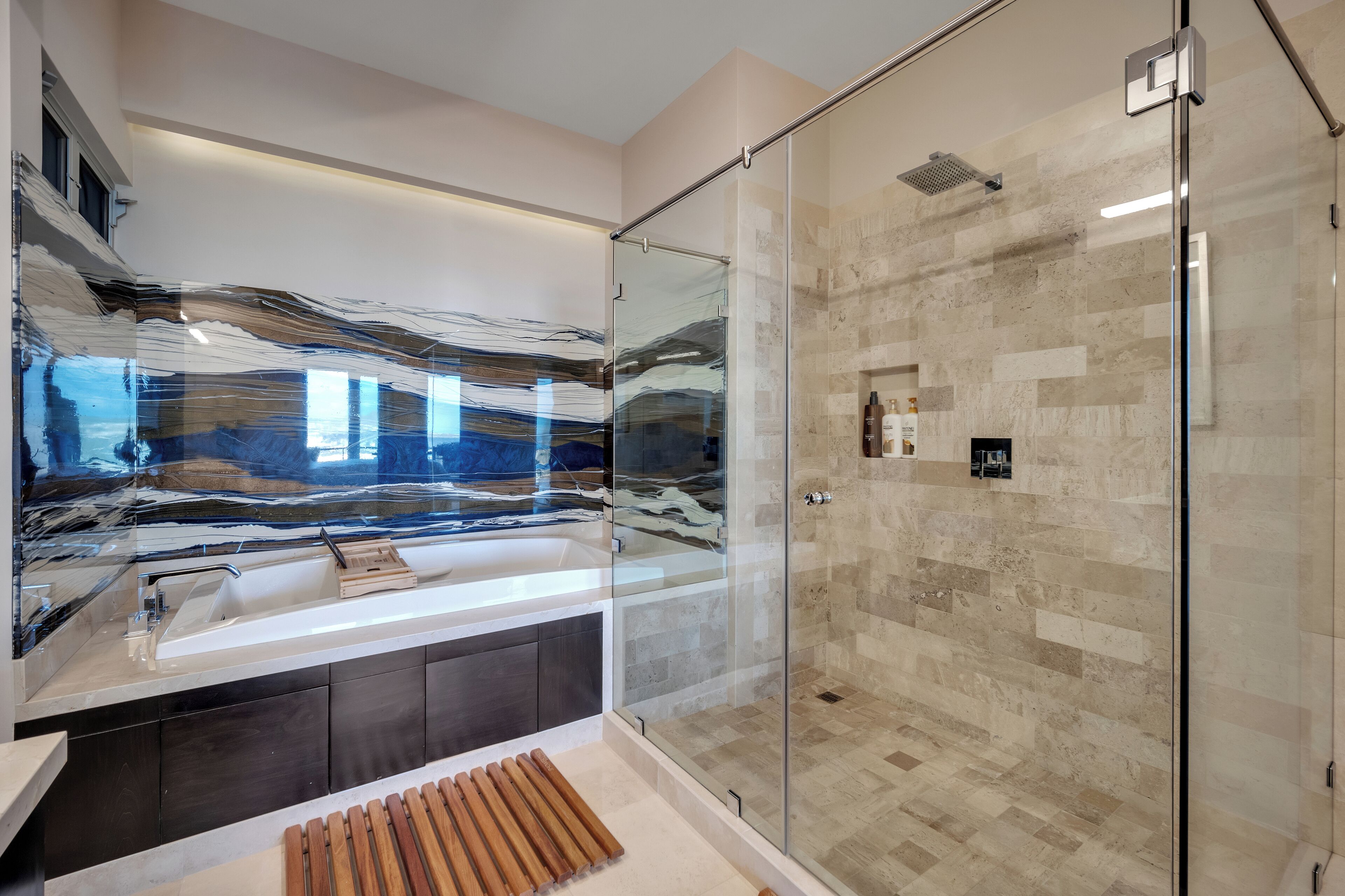 A modern bathroom with a glass shower enclosure, a large mirror, and a wooden bath mat.