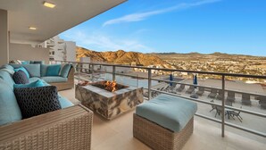 A balcony with a fire pit, wicker furniture, and a view of the city and mountains. - Luxury Cabo Condo in Pedregal, 2 bedroom, 2 bath, City & Ocean Views (Cabo San Lucas)