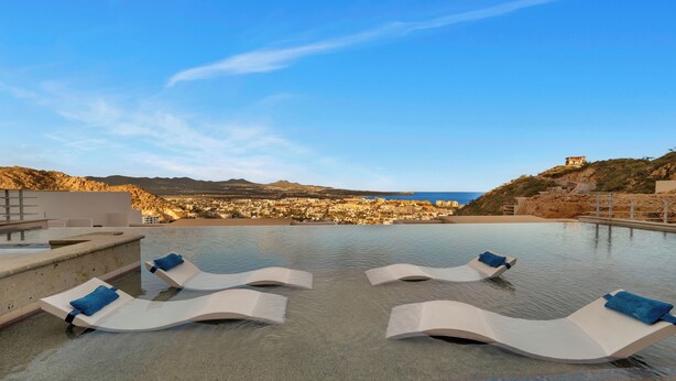 A pool area with lounge chairs and a view of a coastal town. - Luxury Cabo Condo in Pedregal, 2 bedroom, 2 bath, City & Ocean Views (Cabo San Lucas)