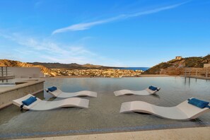 A pool area with lounge chairs and a view of a coastal town. - Luxury Cabo Condo in Pedregal, 2 bedroom, 2 bath, City & Ocean Views (Cabo San Lucas)