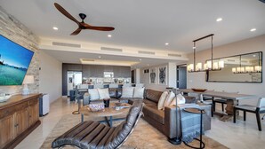 A spacious living area with a modern kitchen in the background, a dining area with a large table, and a ceiling fan. - Luxury Cabo Condo in Pedregal, 2 bedroom, 2 bath, City & Ocean Views (Cabo San Lucas)