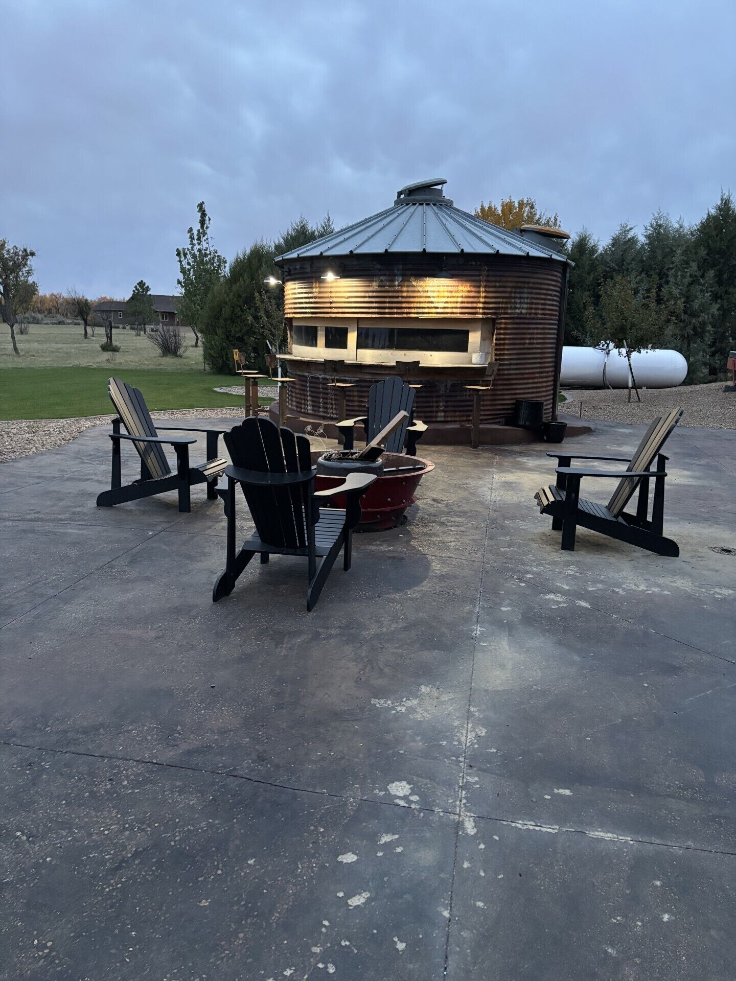 A rustic outdoor seating area with Adirondack chairs and a fire pit, surrounded by a wooden cabin with a metal roof.