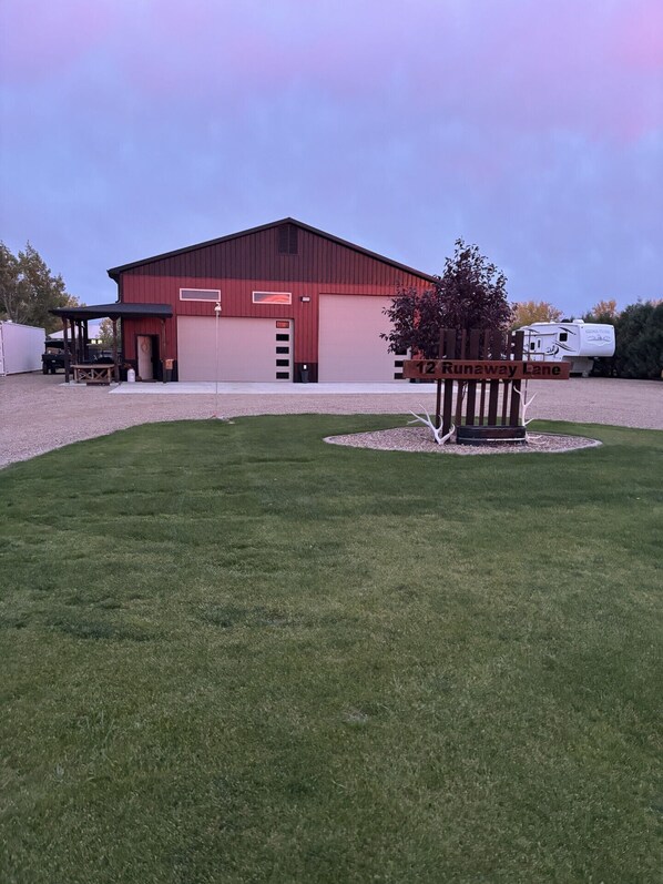 A red barn with a covered area and a white RV parked in front.
