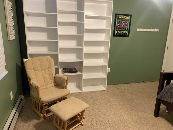 A room with a beige armchair and ottoman, a white shelving unit, a green wall, and a poster saying "Everyone is welcome here." - Emerald Isle Getaway - Tremendous 3-bedroom house with WiFi in Kodiak (Kodiak)