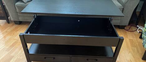 Una sala de estar moderna con un sofá gris, una mesa de centro negra con cajón oculto y suelo de madera.