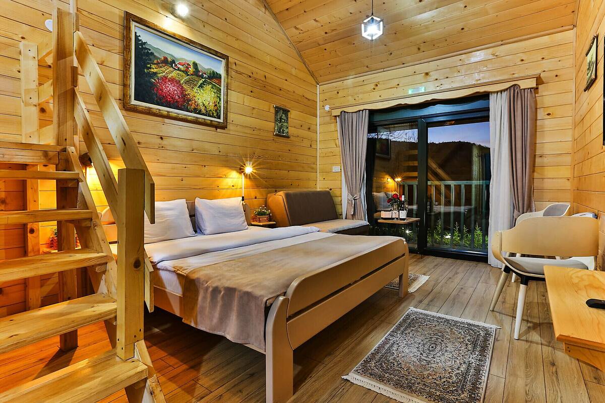 Un dormitorio de cabaña de madera con cama, una silla, un escritorio, una escalera y un balcón con cortinas.