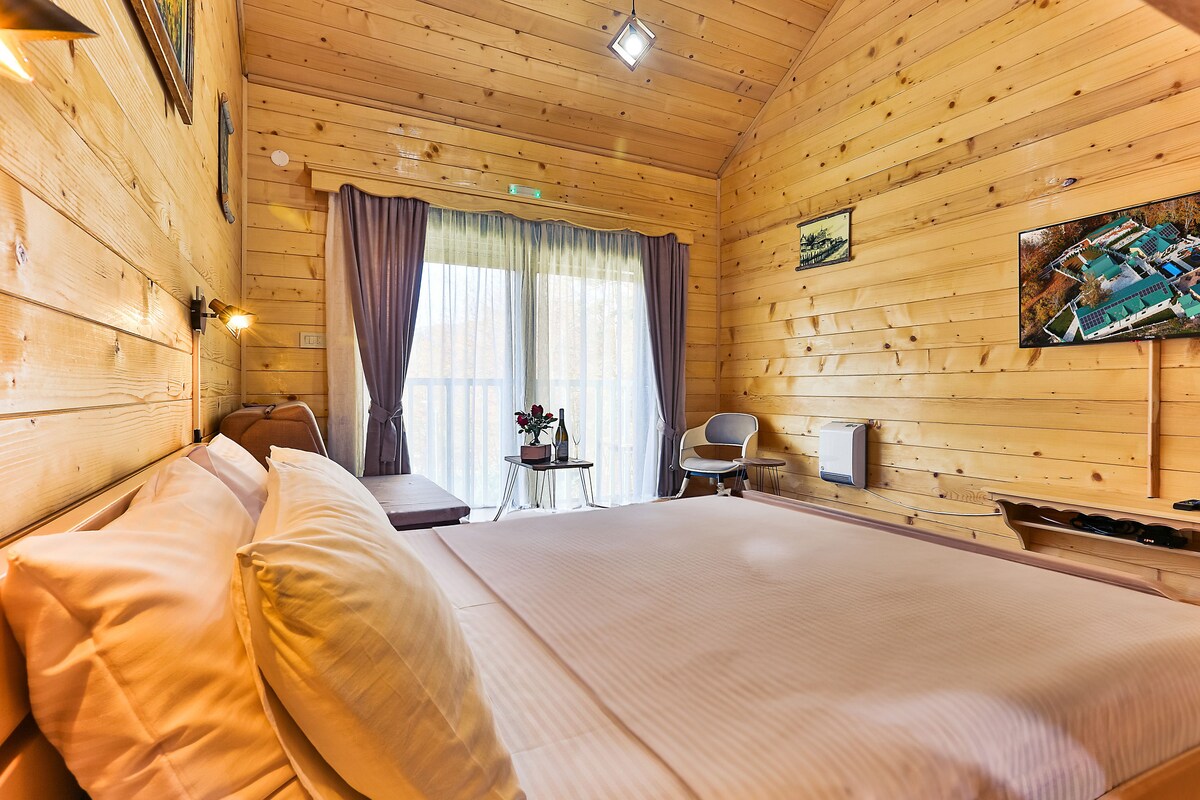 A wooden-paneled room with a bed, a desk, a chair, and a painting on the wall.