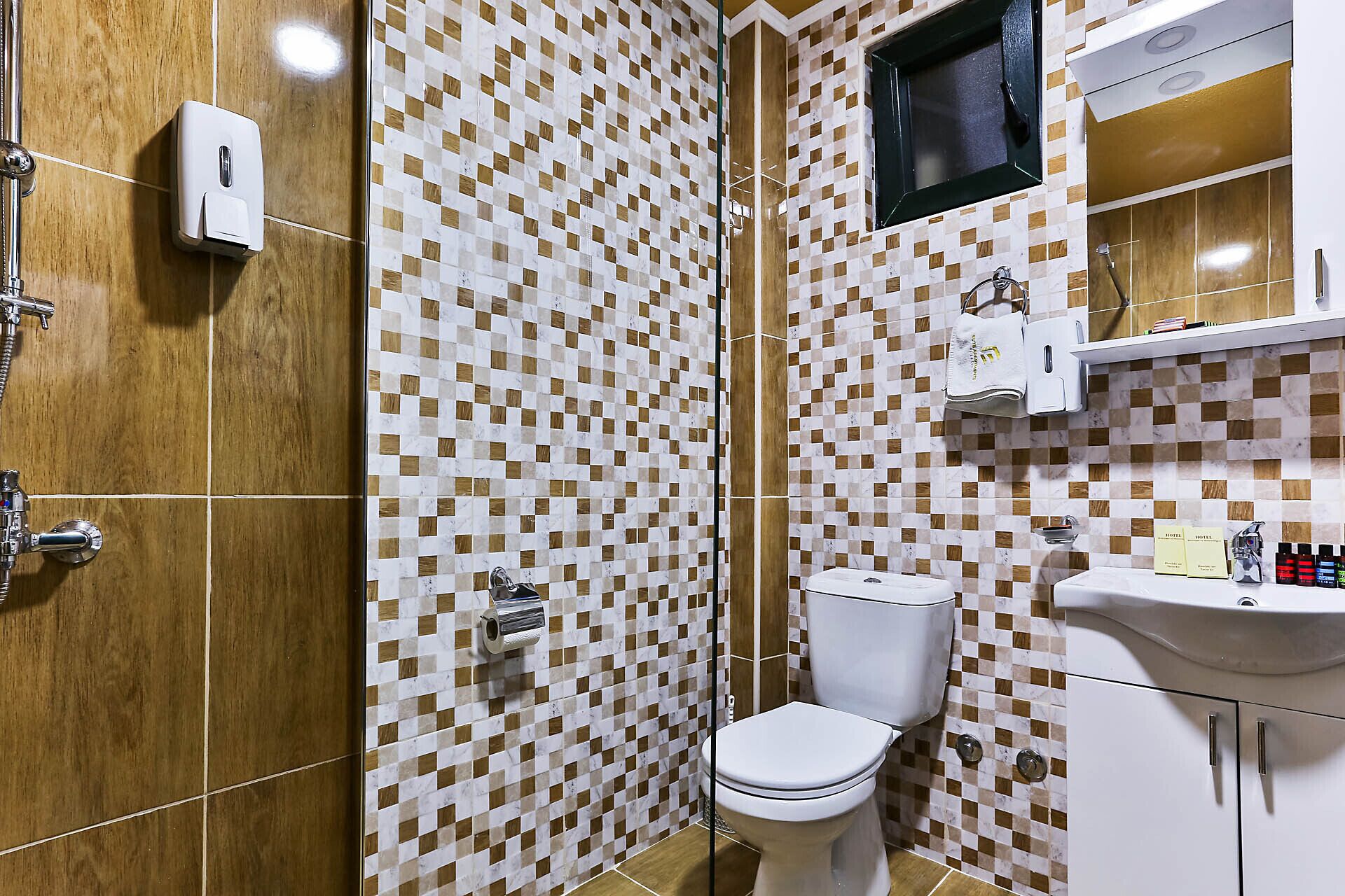 A bathroom with a checkered tile wall, a toilet, a sink, and a shower with a handheld showerhead.