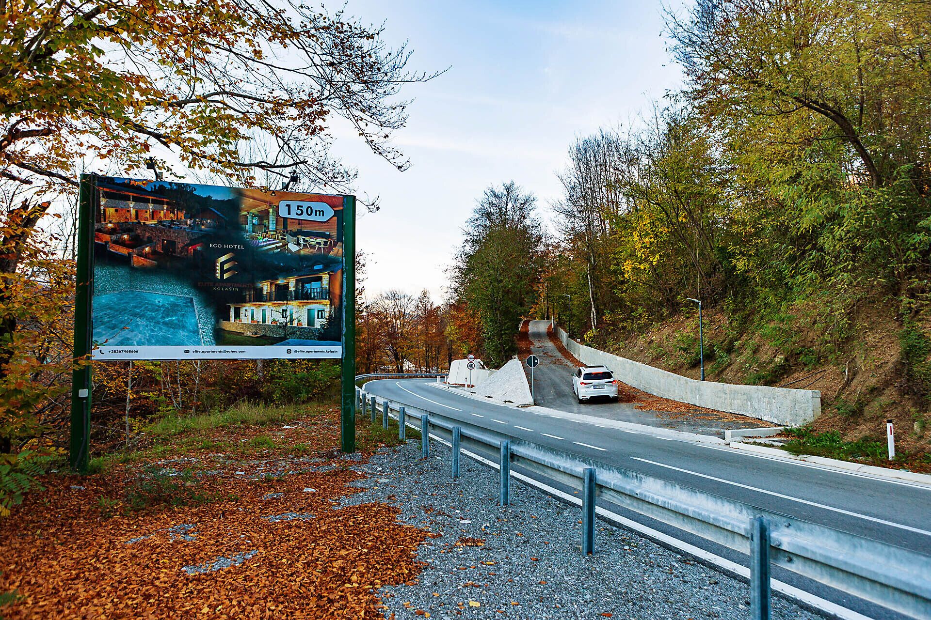 A road sign advertising the Eco Hotel 150m ahead, with a view of a building and a pool.