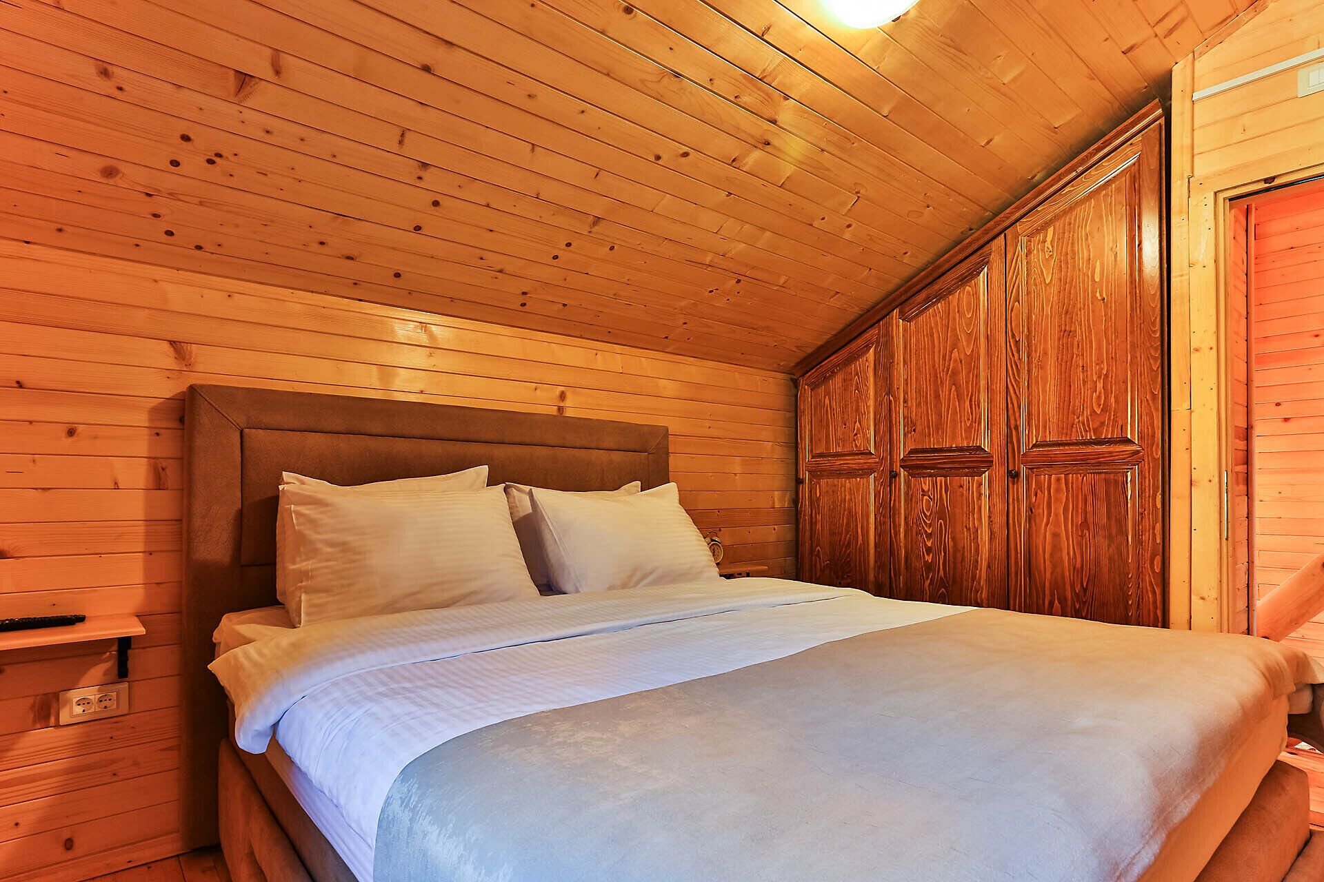 A wooden cabin room with a bed, a nightstand, and a wardrobe.