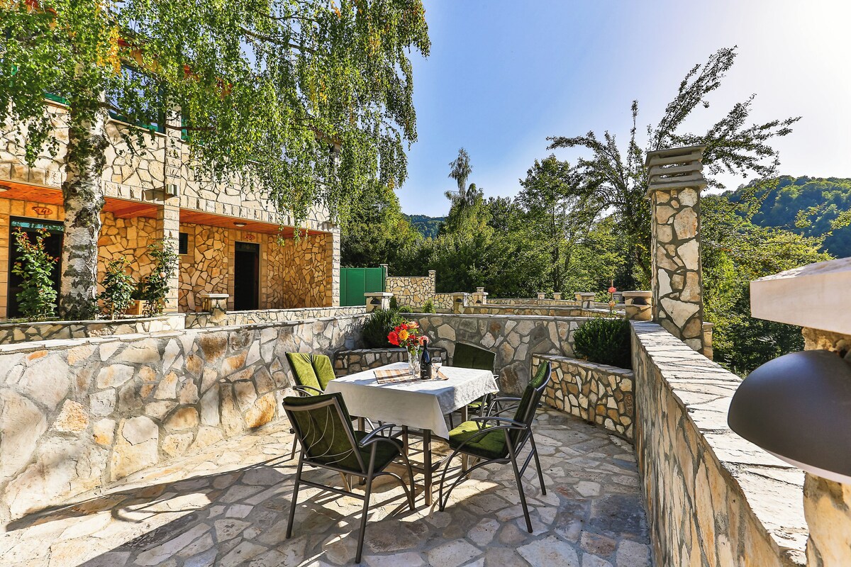A stone patio with a table and chairs, surrounded by stone walls and greenery.