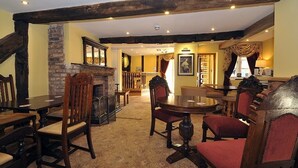 Une auberge traditionnelle avec des poutres apparentes, une cheminée en pierre et un coin salon chaleureux, agrémenté de tables et de chaises en bois.