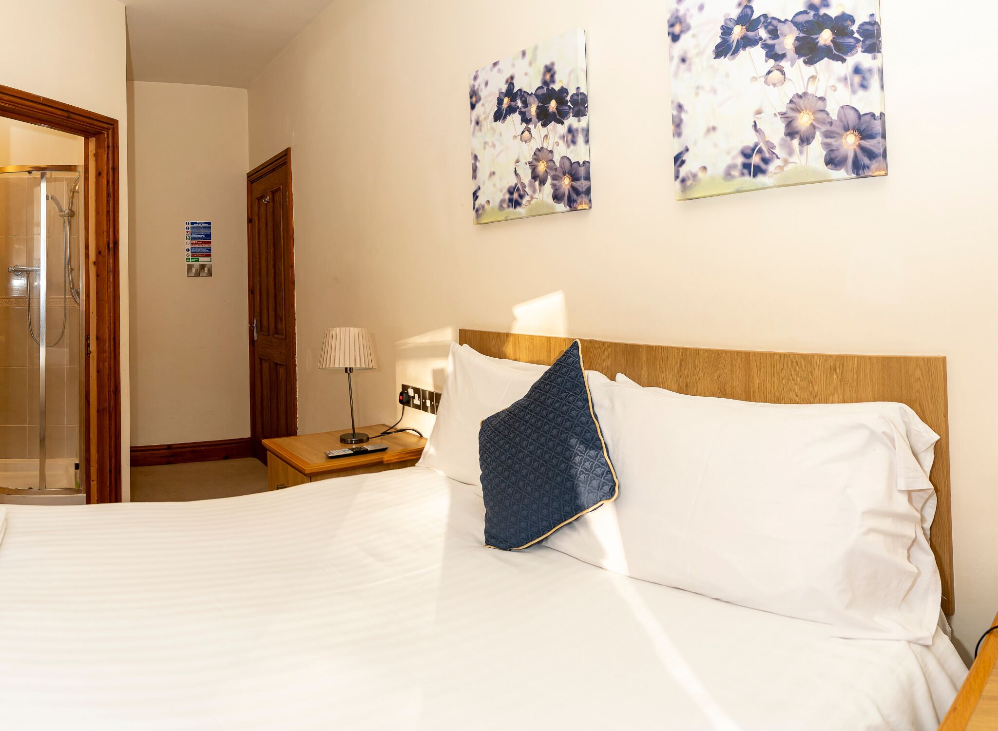 Ein Hotelzimmer mit Bett, Nachttisch, Lampe und einem an der Wand hängenden Gemälde.
