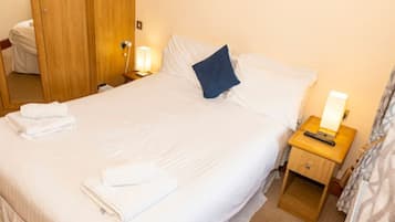A neatly made bed with white linens and a blue pillow, a bedside lamp, and a wooden nightstand with a remote control.