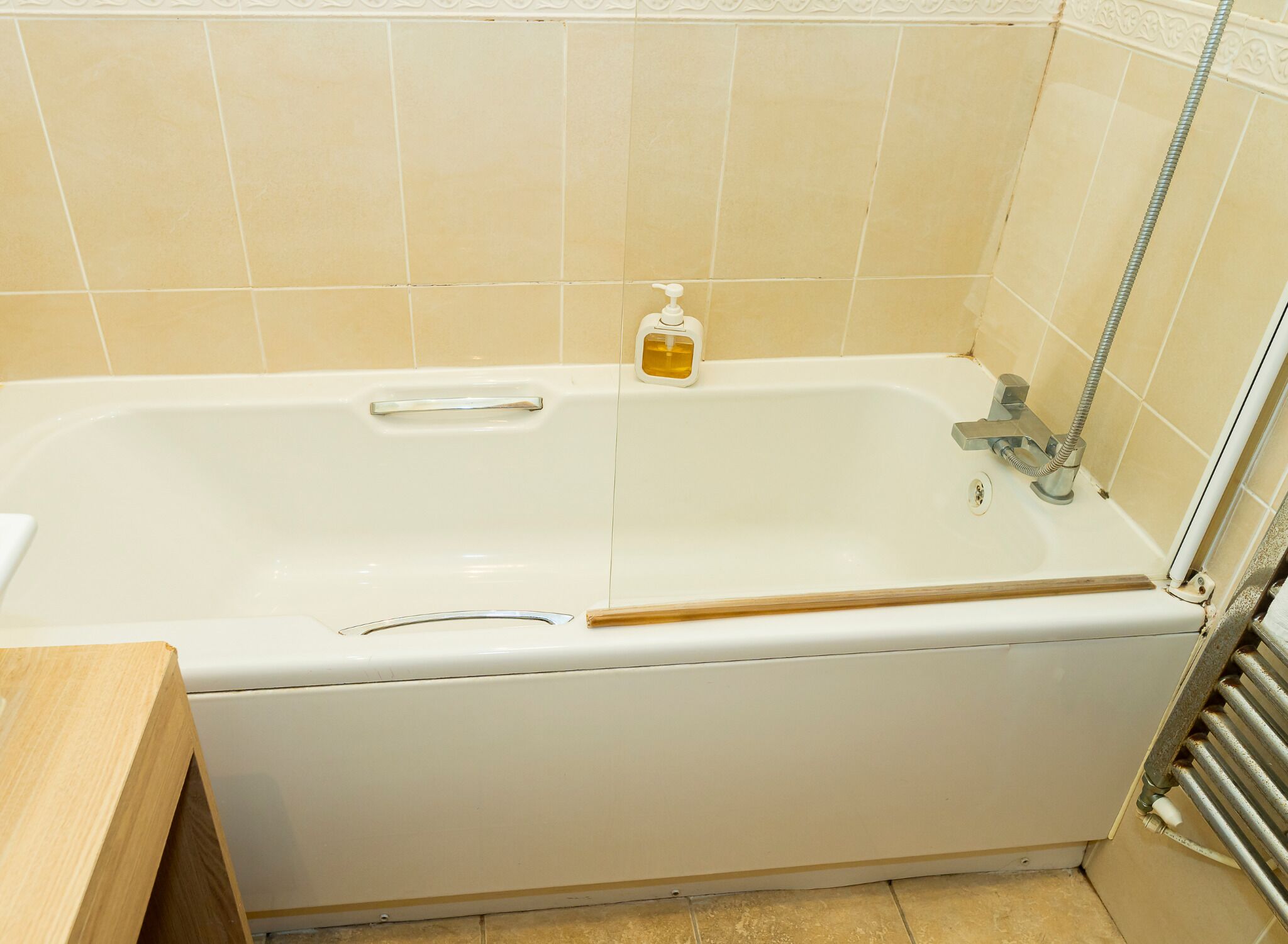 A standard white bathtub with a handheld showerhead, a soap dispenser, and a metal faucet.