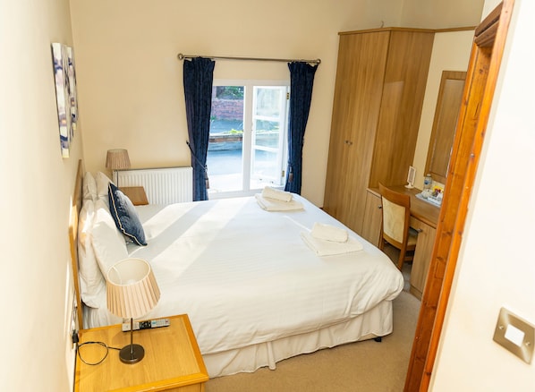 A bedroom with a bed, bedside table, lamp, and a view of the outdoors through a door.