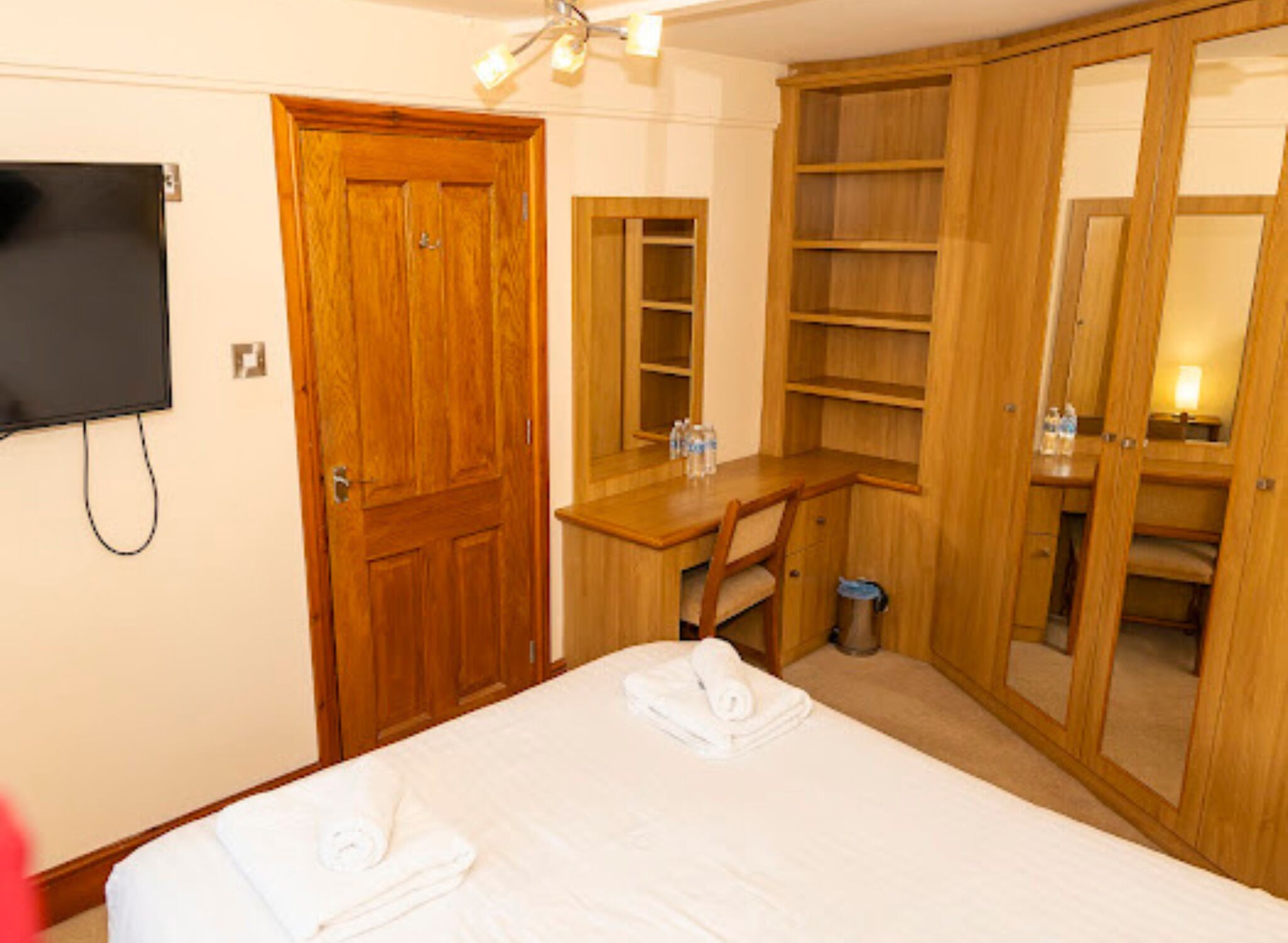 A hotel room with a bed, a desk, a chair, a TV, and a wardrobe.