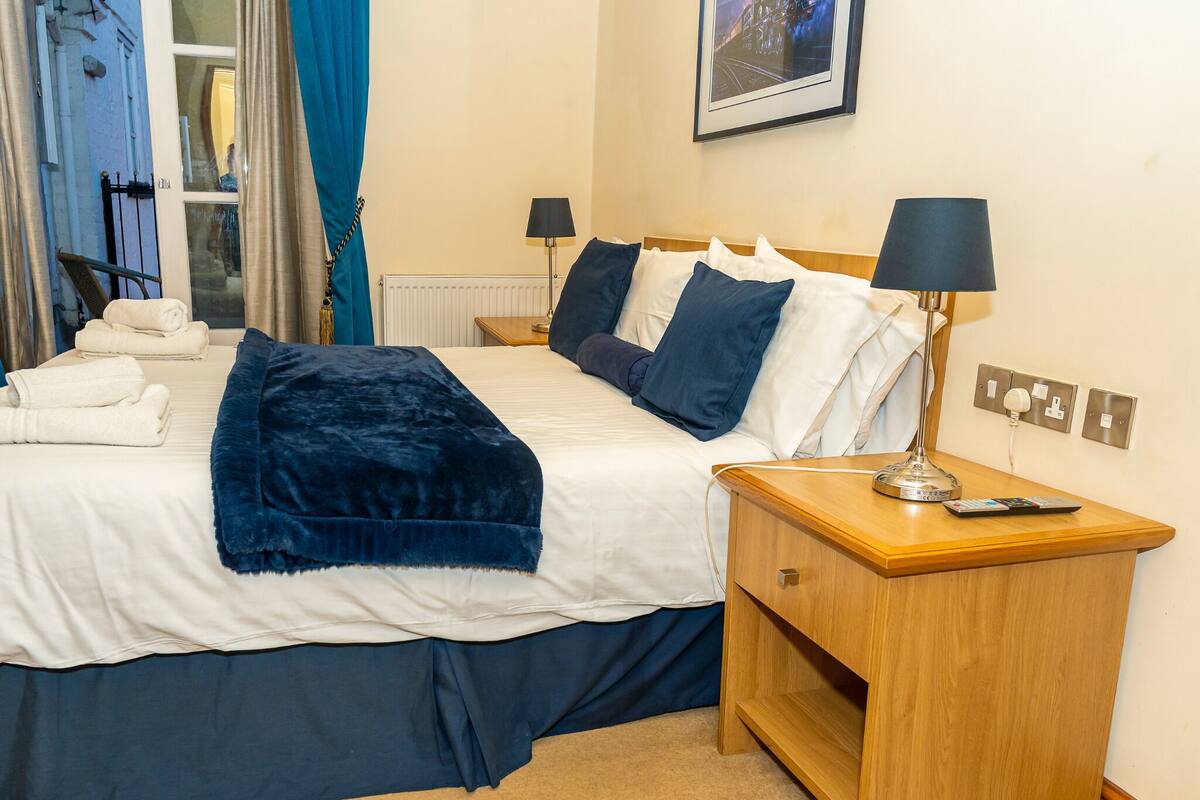 A hotel room with two beds, a wooden nightstand, a lamp, and a framed picture on the wall.