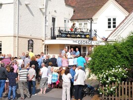 Un pub llamado "The George" con un balcón y un cartel anunciando "Great Ales Served Here".