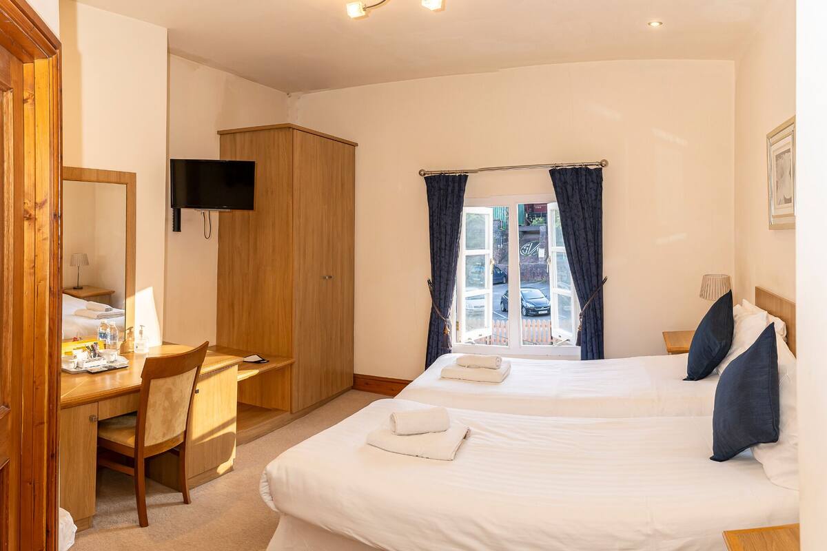 A hotel room with a bed, a desk, a chair, a television, and a window with curtains.