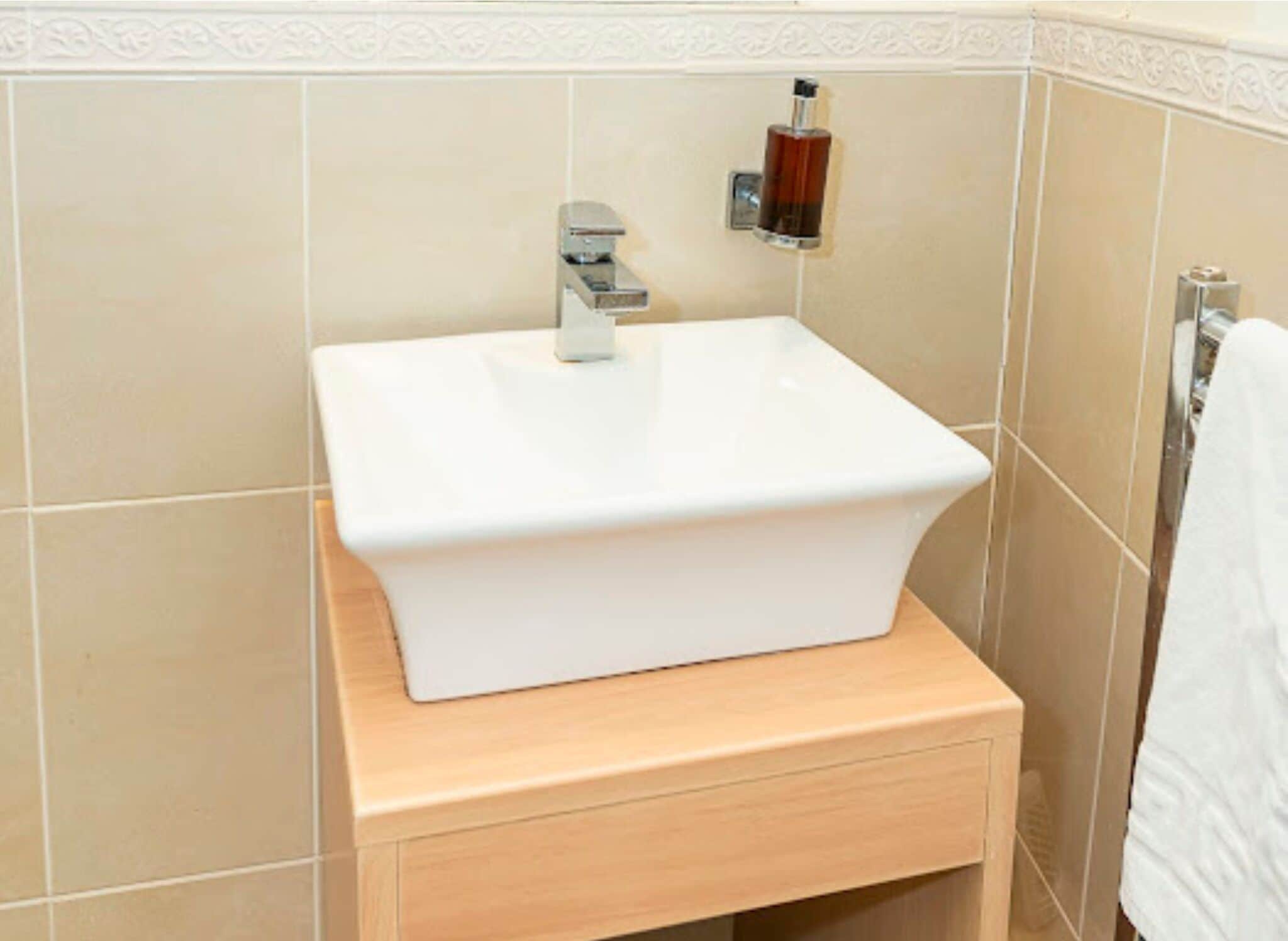 A bathroom with a white sink, a wooden vanity, beige tiles, and a towel hanging on the wall.