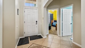 A hallway with a white door, a small window, and a door leading to a room with a bed and a blue wall. - The Minnion's Palace Villa (Kissimmee)
