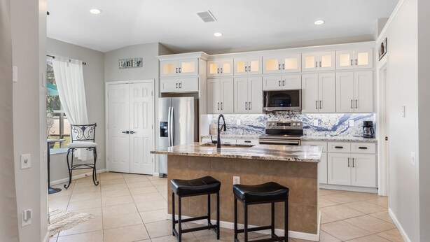 A modern kitchen with white cabinets, a granite countertop, and two bar stools. - The Minnion's Palace Villa (Kissimmee)
