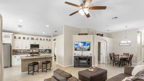 A modern kitchen with white cabinets, a central island, and a dining area with a chandelier. - The Minnion's Palace Villa (Kissimmee)