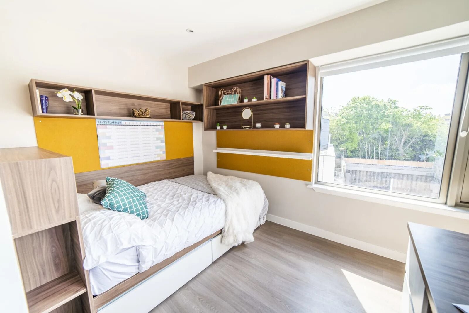 A bedroom with a bed, built-in shelves, a desk, and a window with a view.