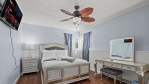 A bedroom with a bed, nightstands, a dresser, a mirror, a ceiling fan, and a TV mounted on the wall.