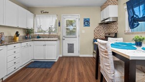 A kitchen with white cabinets, a door with a window, a stove, and a dining area with a table and chairs.