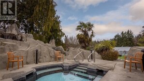 A swimming pool with a tiled deck, surrounded by rocks and palm trees. - Serenity on the Bay - Studio (Nanoose Bay)