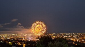 Un paisaje urbano nocturno con un gran espectáculo de fuegos artificiales circulares en el centro.