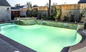 A swimming pool with a stone wall and a wooden fence in the background.